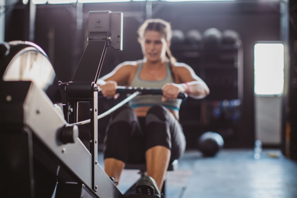 Home young woman on rowing machine in gym